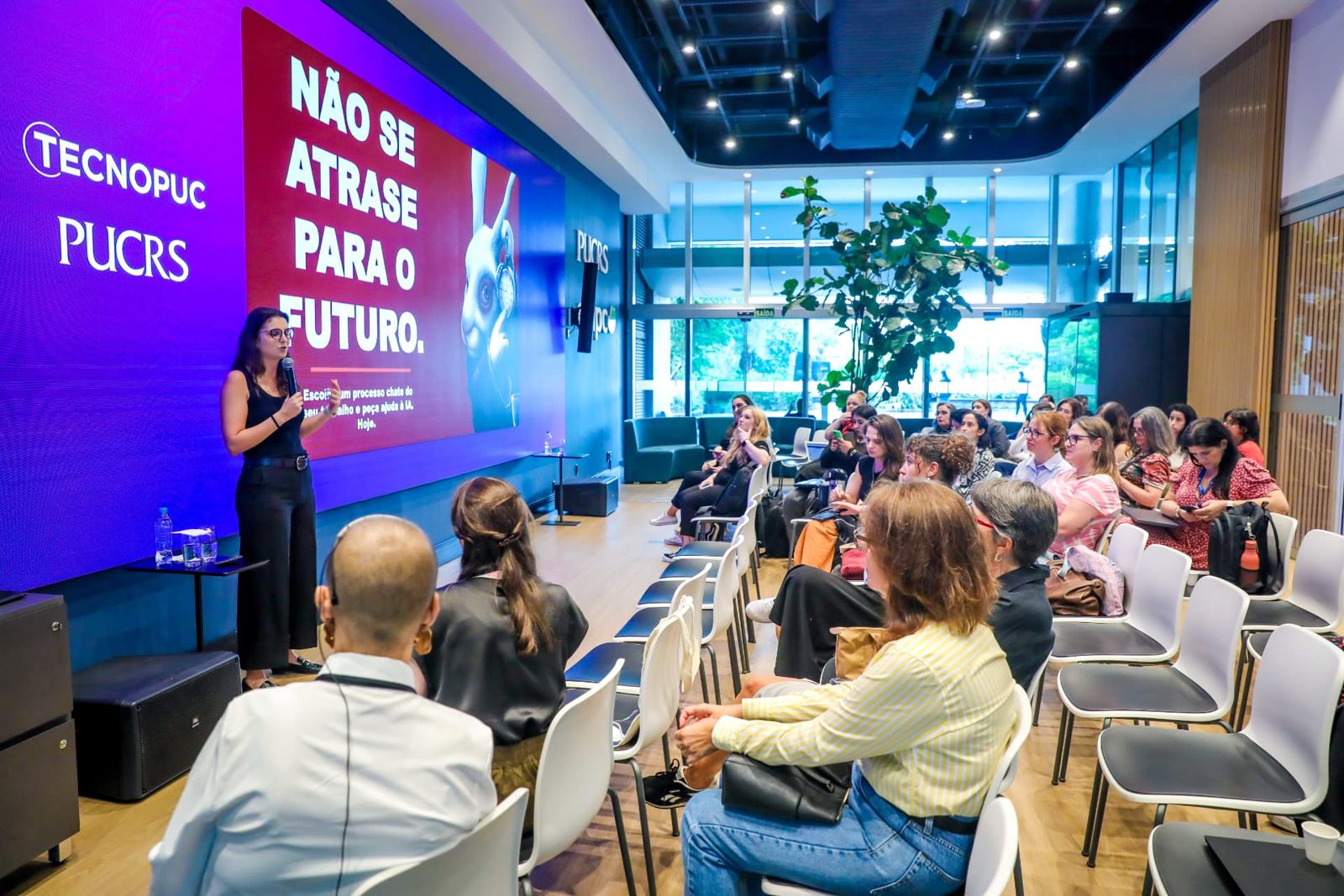 Palestrante fala ao microfone diante do slide "Não se atrase para o futuro".